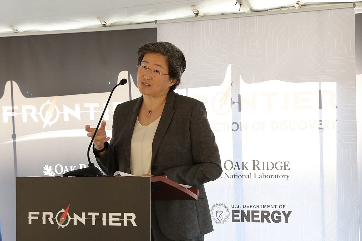 Lisa Su in glasses and a grey jacket speaking at a lectern marked Frontier, with Oak Ridge National Laboratory and Department of Energy banners behind her