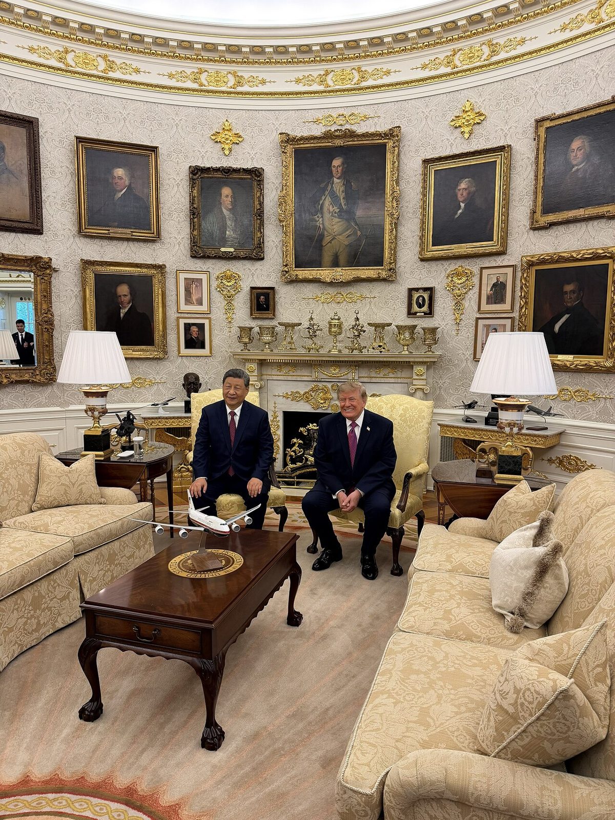 Xi Jinping and Donald Trump seated in yellow armchairs before a fireplace, under a wall of gilt-framed portraits