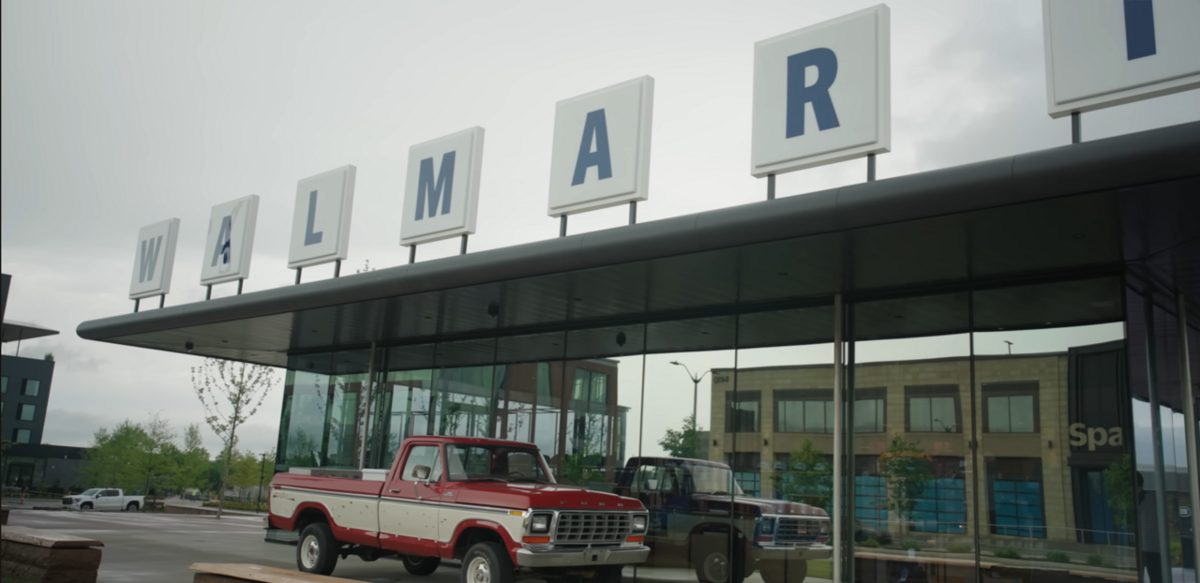 A glass pavilion under large white letter signs spelling Walmart, with a red and white vintage pickup truck parked in front