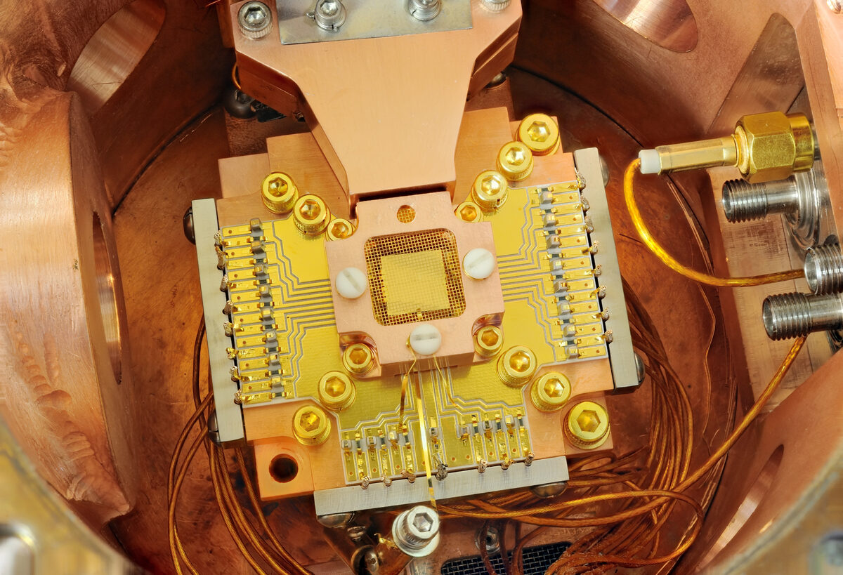 A gold-plated chip at the center of a copper vacuum chamber, surrounded by fine wires and connectors.